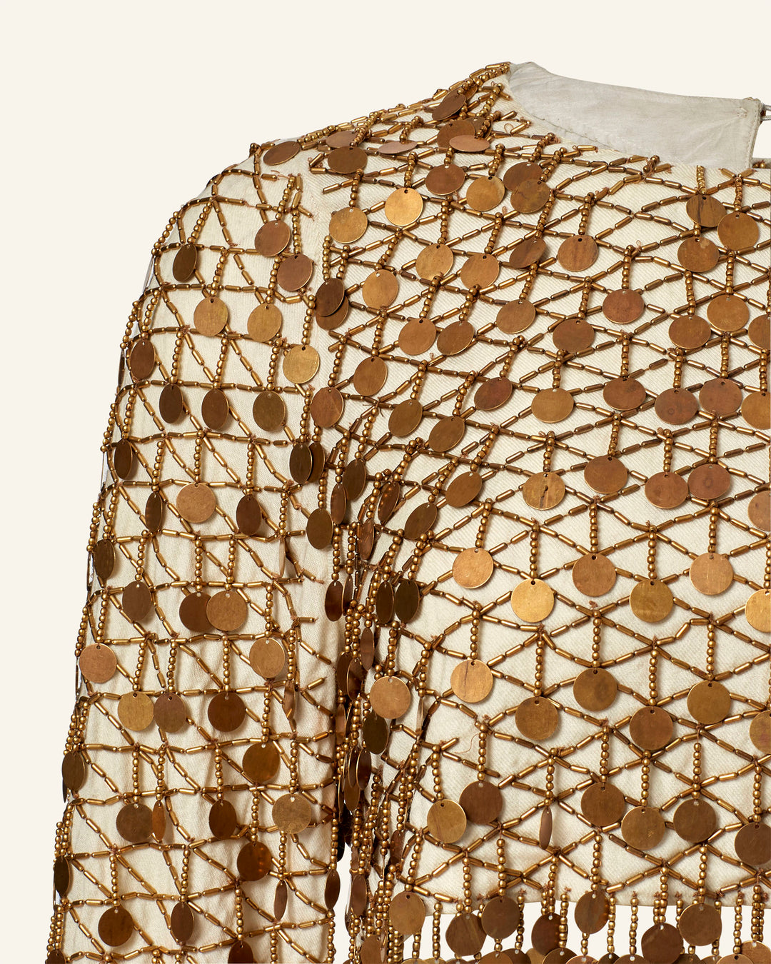 Close-up of the Nina Whitegold Coin Top, a hand-embellished cropped top with a netted overlay, gold discs, and twisted gold cords on a light fabric background.