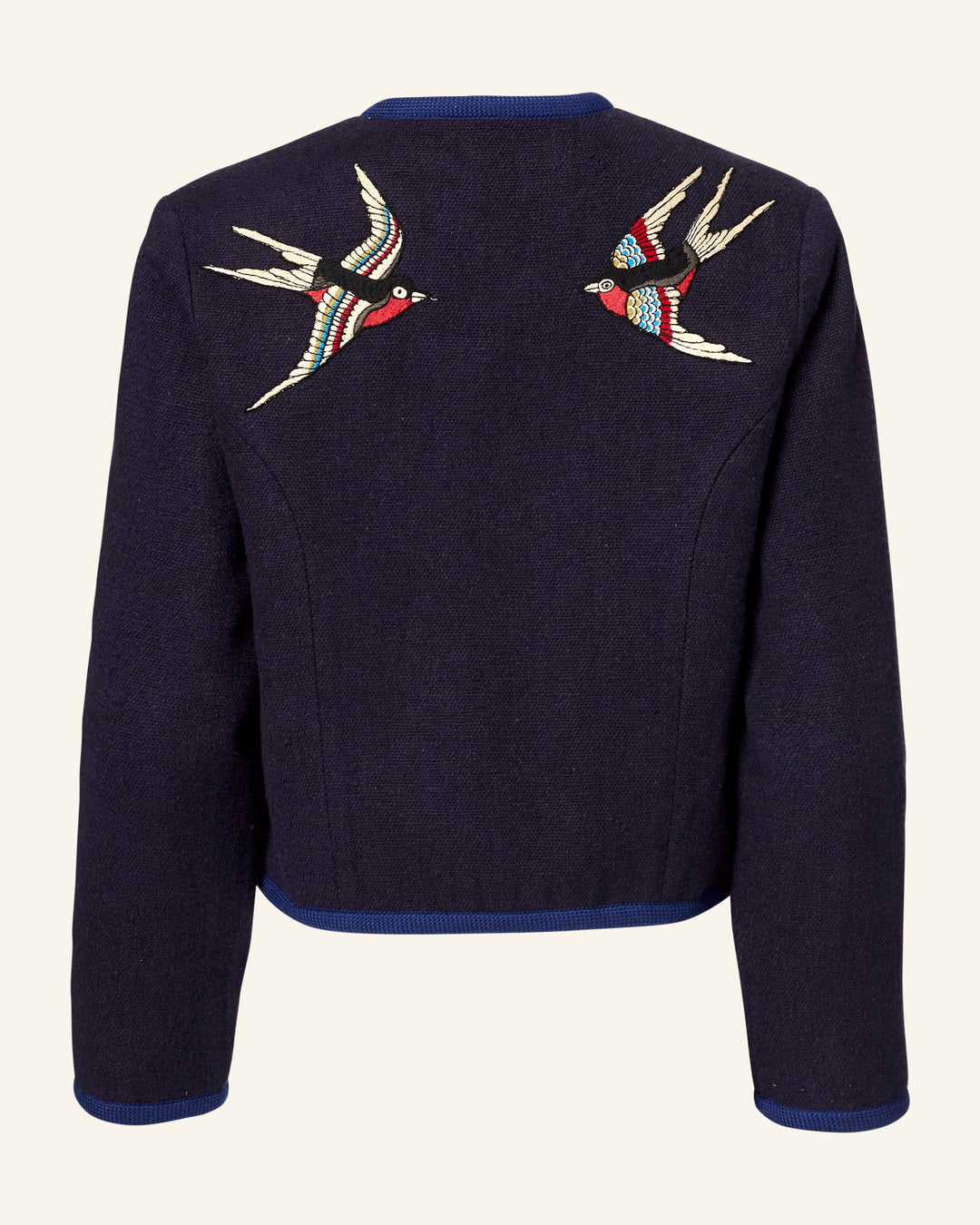 The Rowan Midnight Swallow Jacket is a dark blue Khadi cotton jacket featuring a bright blue trim on the collar and hem, with two symmetrically placed hand-embroidered birds in flight on the back, showcasing colorful artisanal patterns.