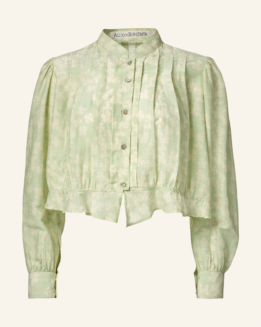 The Ryland Celadon Clover Shirt is a light green floral blouse with long sleeves, a high collar, and button-up front. It has a slightly cropped, ruffled hem and features a cotton-silk blend fabric with soft texture and floral patterns reminiscent of a Victorian silhouette.