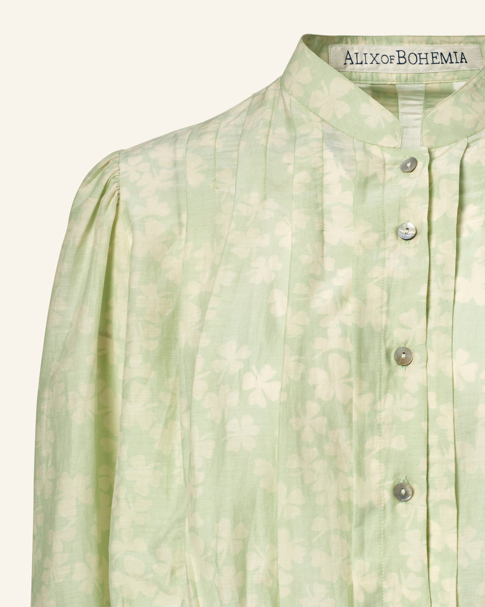 Close-up of the Ryland Celadon Clover Shirt, a light green blouse with a subtle floral pattern, high collar, and button-down front. Crafted from a luxurious cotton-silk blend with hints of Victorian silhouette, labeled "Alix of Bohemia.