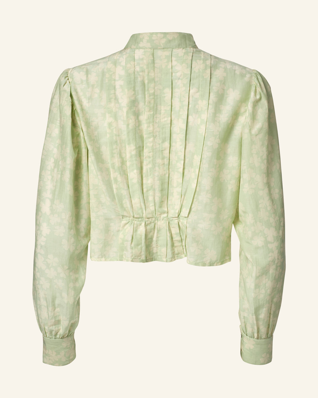 The Ryland Celadon Clover Shirt, in a light green cotton-silk blend, features a floral pattern and Victorian silhouette. It has a structured back with vertical pleats, slightly cinched waist, subtle sheen, high neck, and buttoned cuffs.