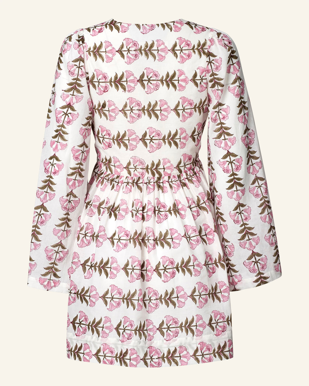 The Silvie Trumpet Lily Dress is a cotton voile, long-sleeved dress featuring pink floral hand-block prints with green leaves. It has a gathered waist, knee-length hemline, and a neutral background.