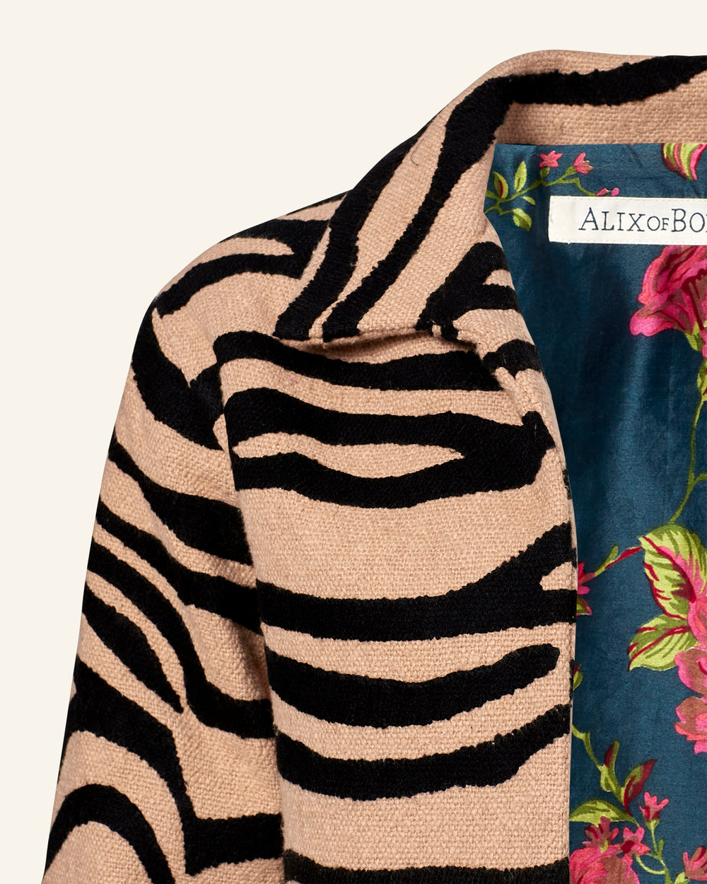 Close-up of the Western Zebra Mirage Jacket: a beige animal print jacket with bold black zebra stripes made from Khadi cotton. The inner lining displays a dark teal background with vibrant pink and green floral patterns. A "ALIX of BOHEMIA" label is elegantly placed near the collar.