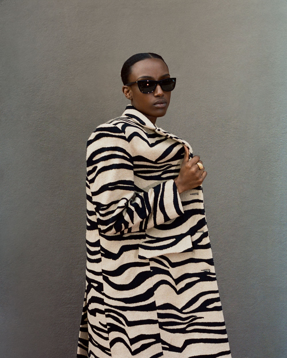 Wearing the Captain Zebra Mirage Coat with bold zebra stripes, paired with dark sunglasses, an individual stands confidently against a plain background.