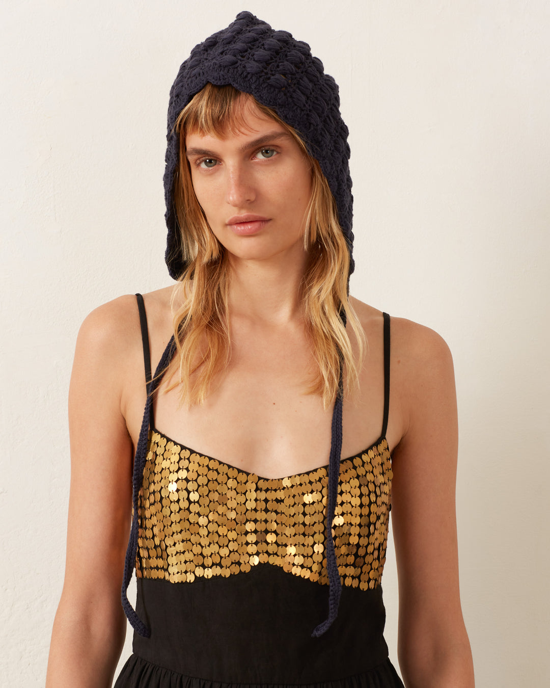 A person wearing a black knit hat and the Autumn Blackjack Coin Dress adorned with gold metal sequins stands against a neutral background.