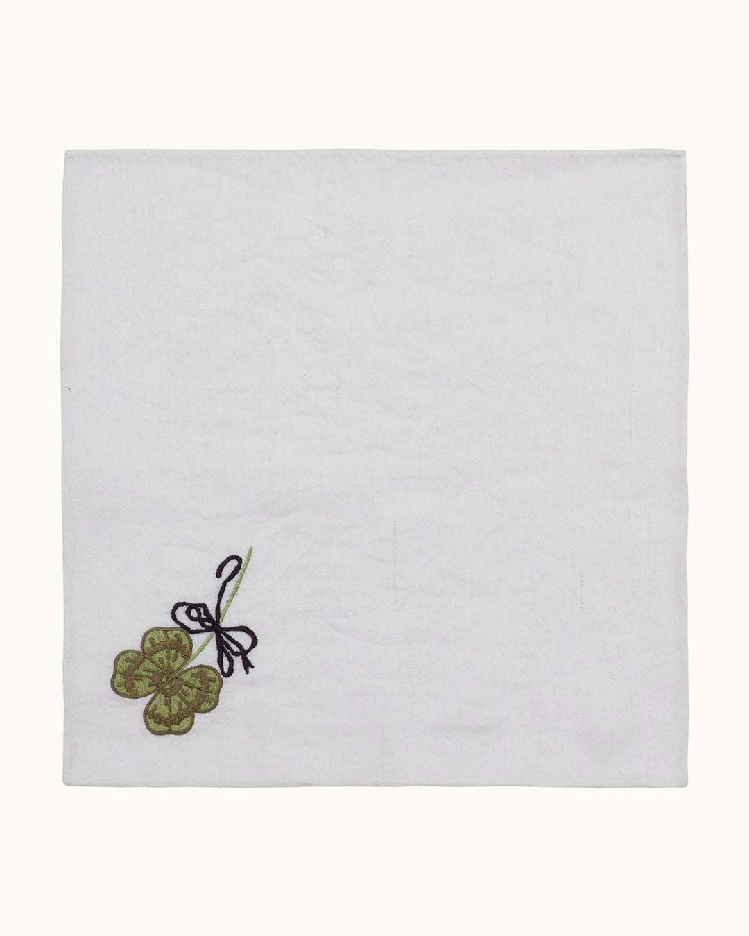 The Cai Lucky Love Handkerchief features a charming design, showcasing a green four-leaf clover and delicate black ribbon beautifully embroidered on a soft linen-cotton blend white cloth.