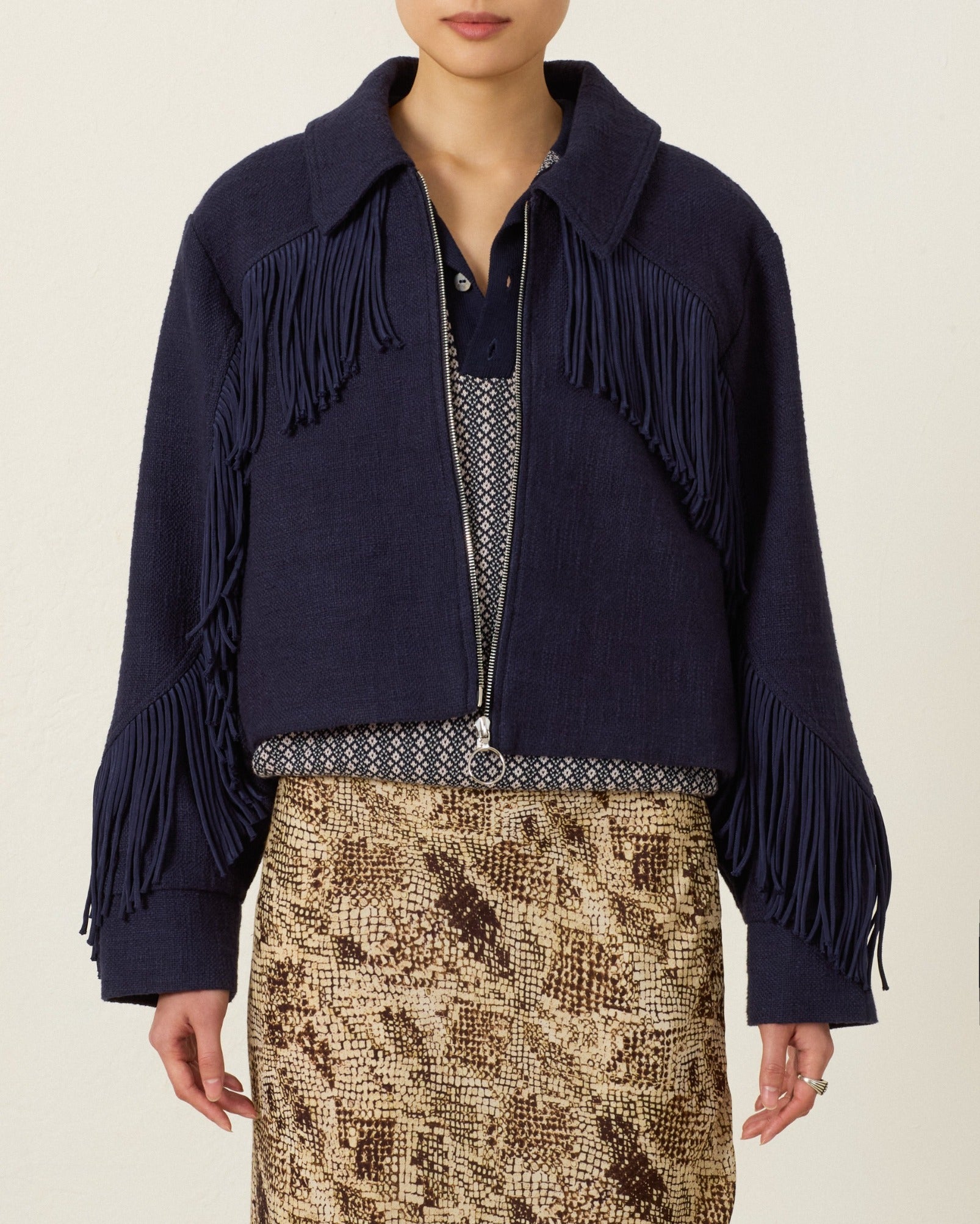 Wearing the Court Indigo Night Jacket—a navy blue khadi cotton piece with Western fringing—over a patterned shirt and a snakeskin-patterned skirt, a person stands against a plain light background.