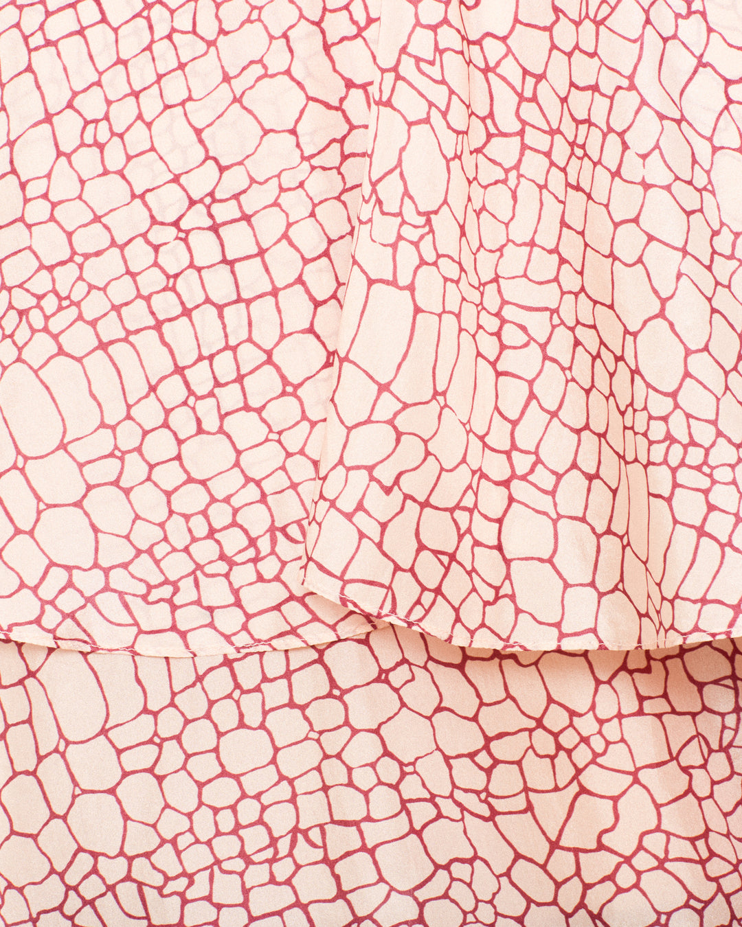 Close-up of the Eleanor Crocodile Silk Shirt, showcasing its hand-loomed silk fabric with a pink, irregular grid-like pattern reminiscent of stones or a subtle crocodile print. Some of the fabric is folded over itself.