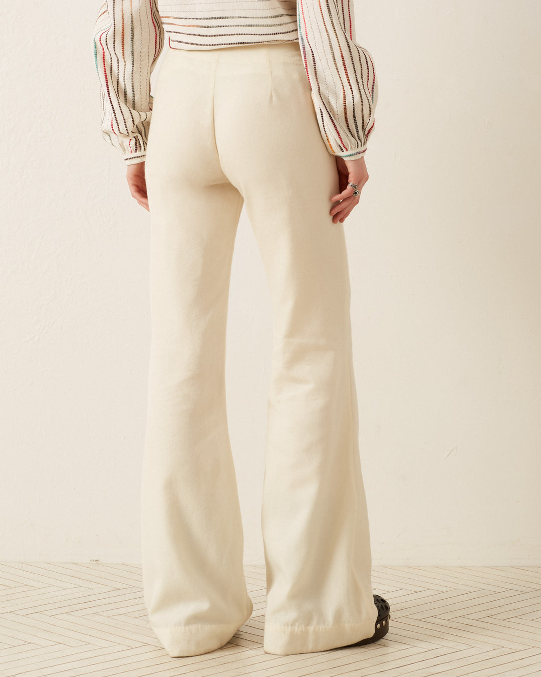 The individual is dressed in the Charlie Ivory Prism Pant, paired with a striped long-sleeve top, standing on a patterned floor against a neutral backdrop.