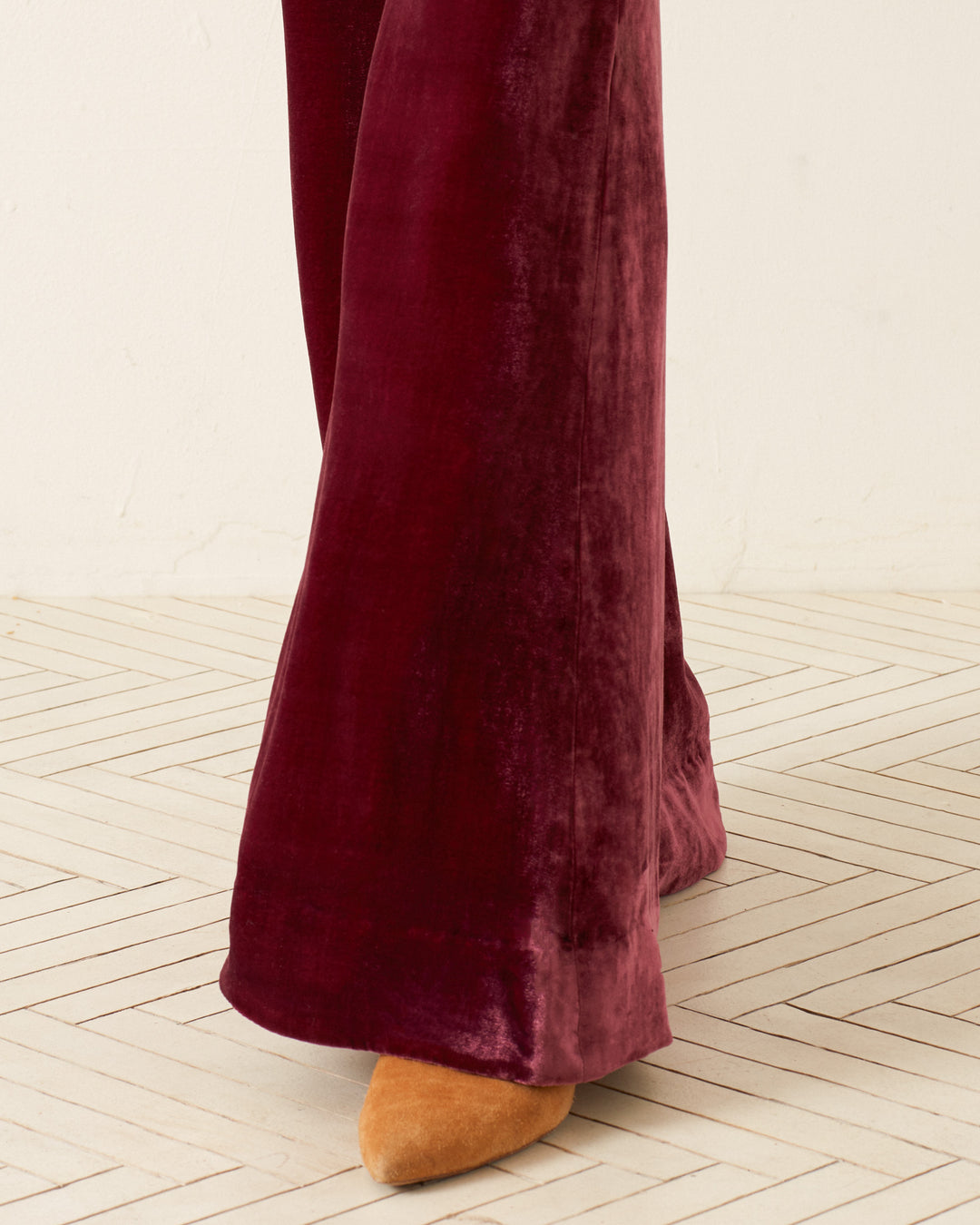 A close-up of a person wearing the Charlie Plum Velvet Pant paired with mustard-colored shoes, standing on a light-colored herringbone-patterned floor. The texture and sheen of the fabric capture attention, evoking a vibrant '70s style vibe.