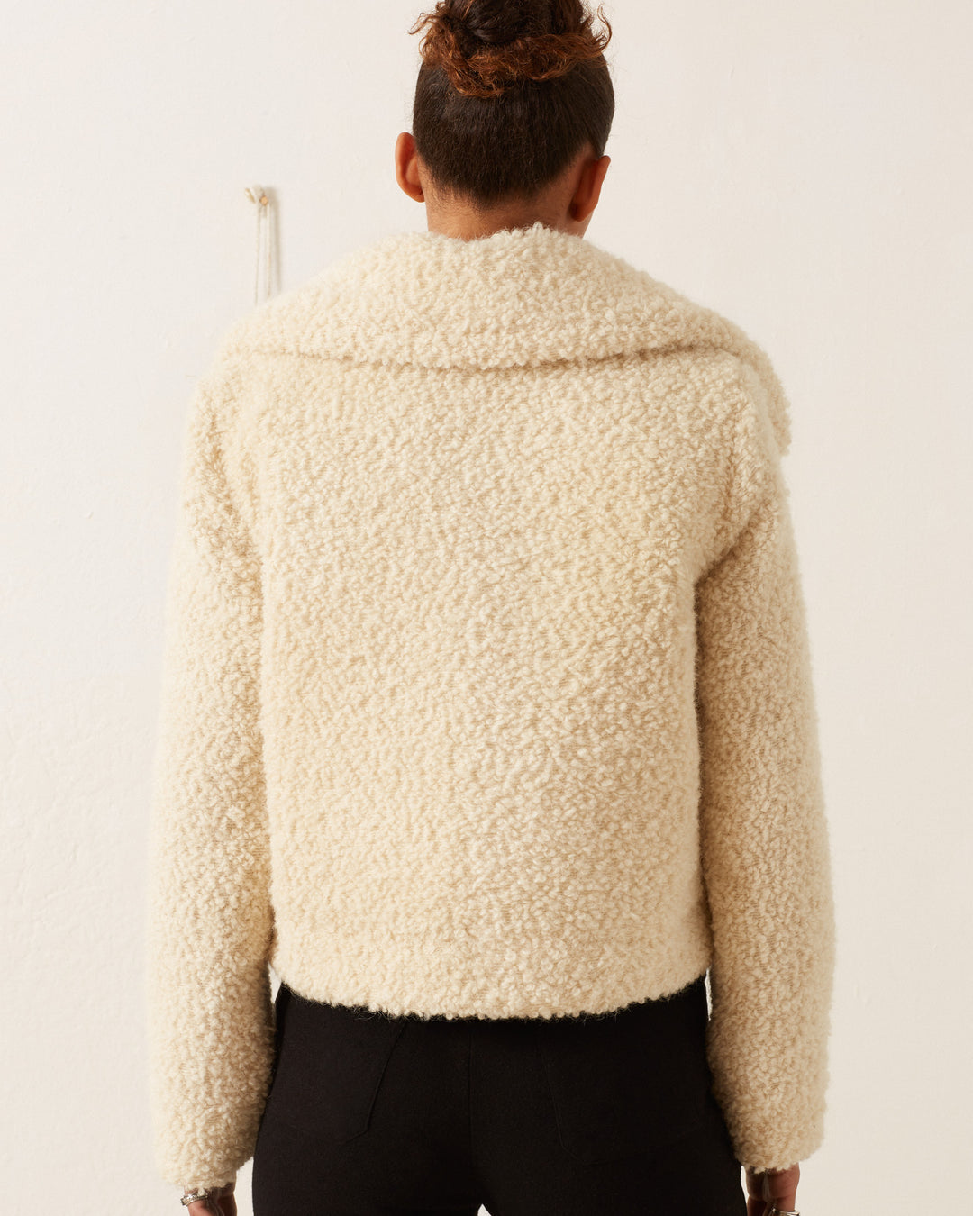 A person with short hair, seen from behind, is wearing the cozy Colby Suri Wool Jacket in a cream shade, featuring an oversized collar and paired with black pants against a plain white background.