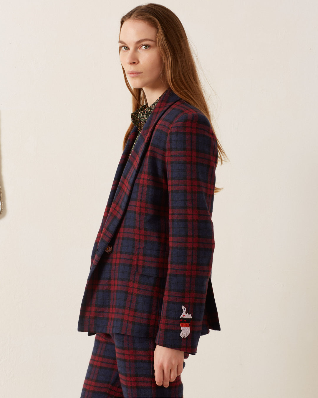 A person with long hair wearing the Dree Berry Plaid Blazer stands against a plain background, its cotton-silk lining adding a touch of elegance to their stylish ensemble.