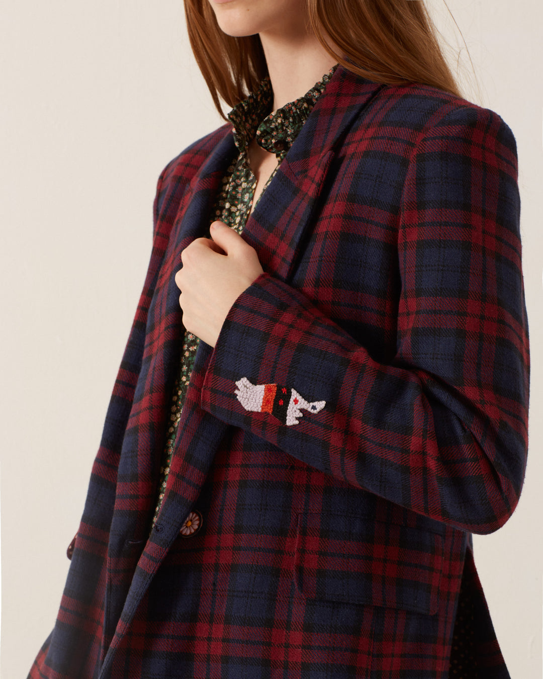 A person wearing the Dree Berry Plaid Blazer, featuring an embroidered dog on the sleeve and a luxurious cotton-silk lining.