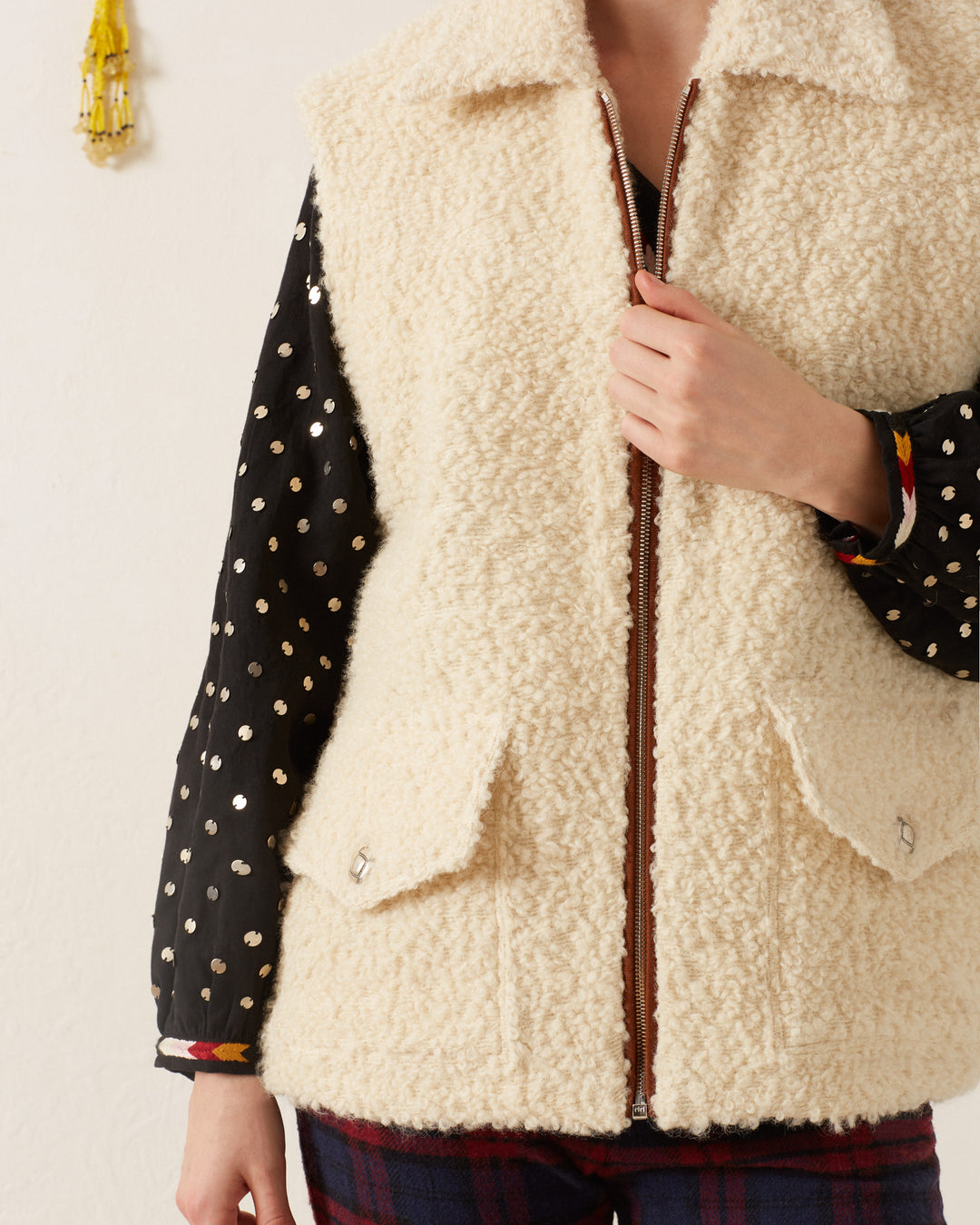 A person is stylishly wearing the Mickey Suri Wool Vest in a creamy hue over a black, gold polka-dotted shirt, perfect for winter layering.