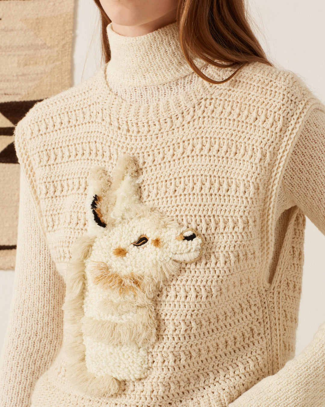 The Oona Llama Crochet Top showcases a cream-colored, hand-embroidered sweater with a charming llama design on the front, accentuated by textured, three-dimensional detailing. This vintage-inspired piece elegantly covers only the upper body.