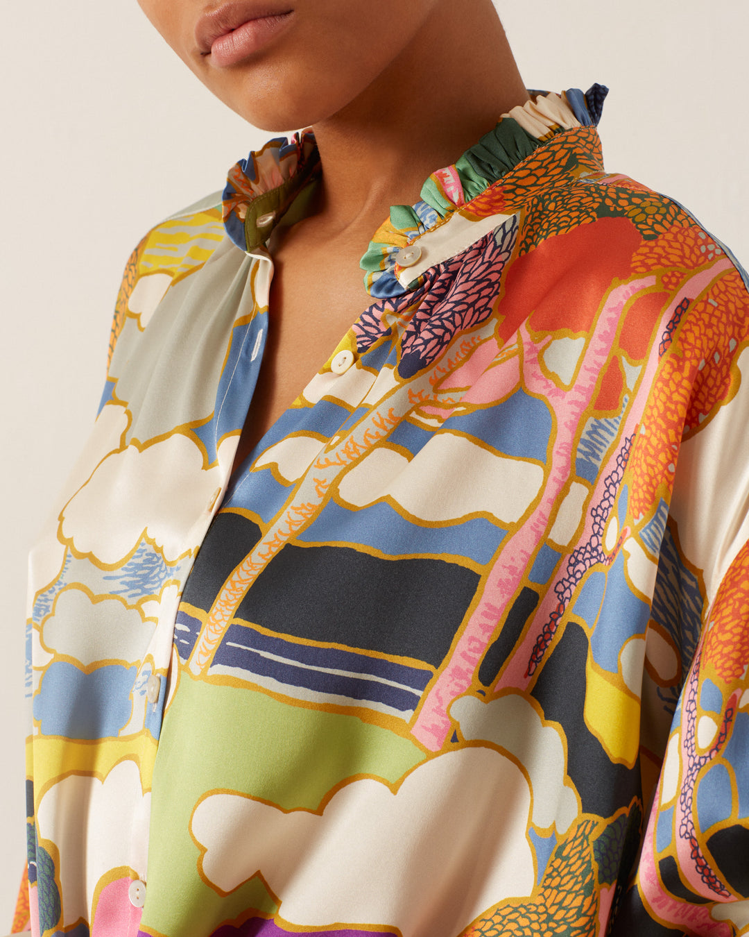 A person wearing the Poet Aurora Silk Blouse, which showcases a vibrant Liberty-print with a ruffled collar adorned with abstract shapes and Art Nouveau landscape designs.