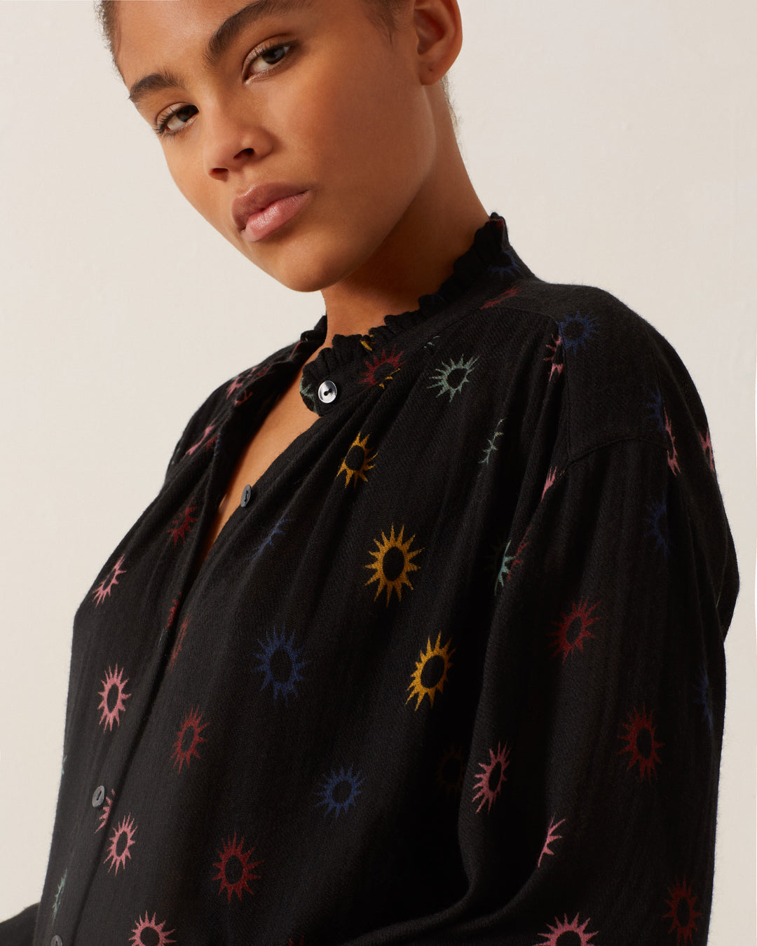 The individual is wearing the Poet Evening Star Blouse, featuring a vibrant starburst design, and is facing the camera against a simple backdrop.