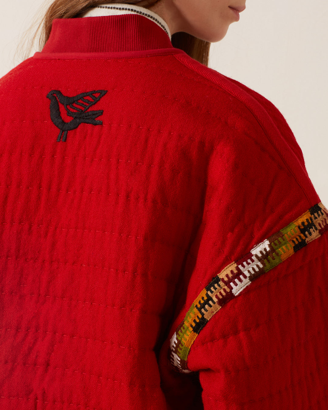 Wearing the Sutton Scarlet Blanket Bomber, with its hand-quilted design, red color, black bird emblem on the back, and colorful sleeve trim, makes a person look strikingly stylish.