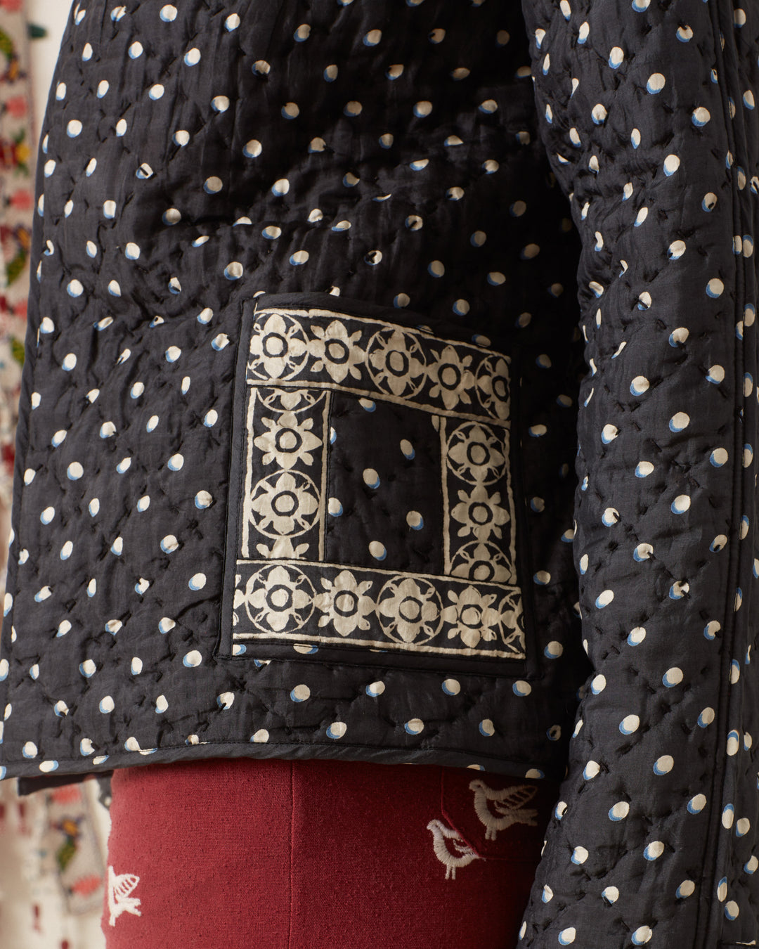 Close-up of the Tamil Raven Dot Silk Jacket, featuring white polka dots and an embroidered pocket, complemented by a stylish tie-belt. This elegant jacket is beautifully paired with red pants adorned with small embroidered designs.