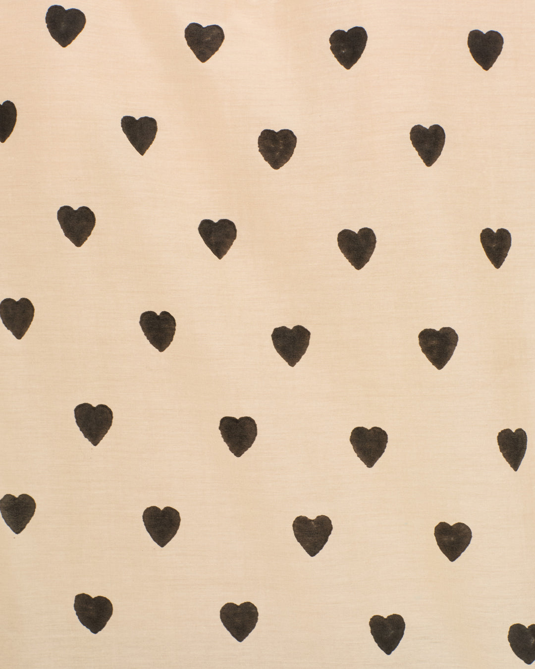 The Artemis Onyx Heart Shirt features a beige fabric background with evenly spaced black heart shapes, evoking the charm of hand-block printing and delicate blouse details.