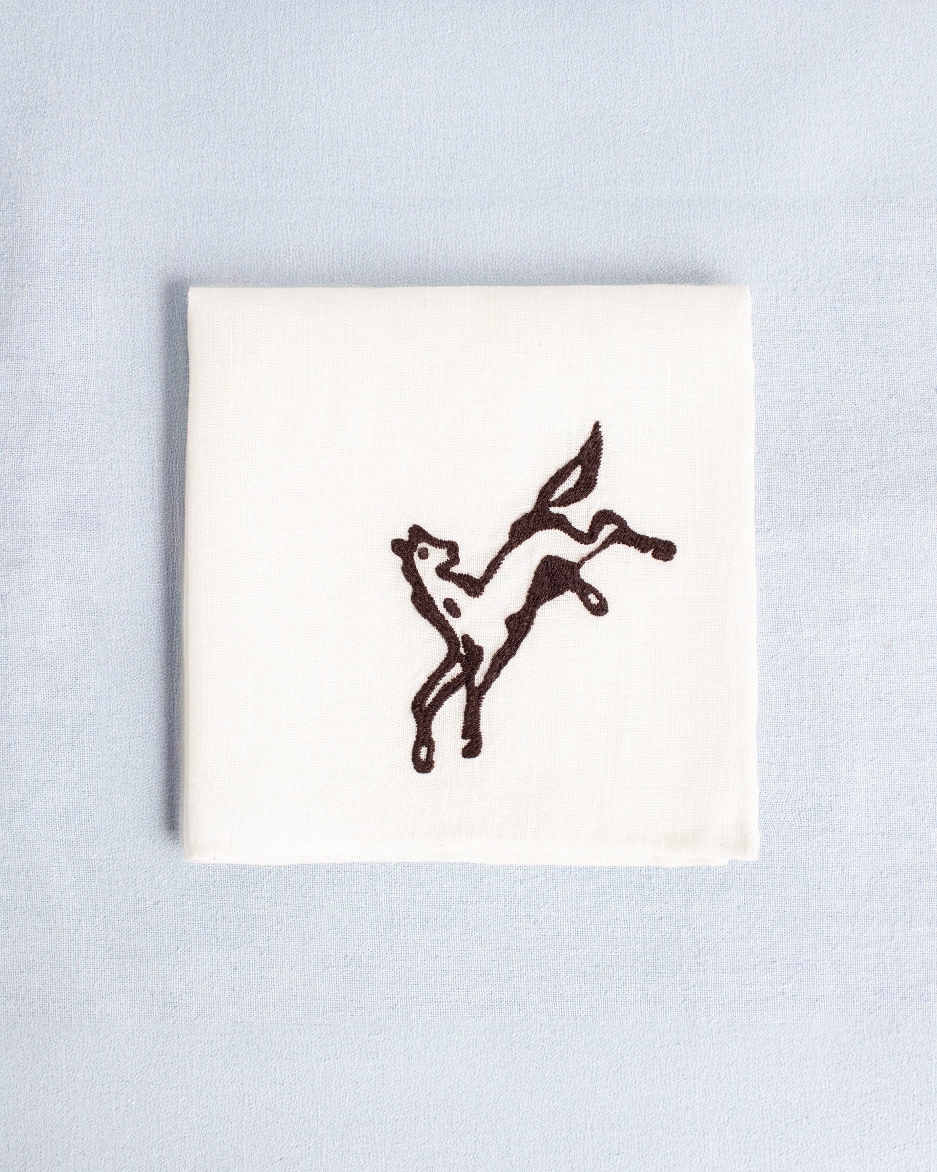 The Cai Bronco Handkerchief is a white linen-cotton accessory with a simple black embroidered prancing horse, shown on a light blue background—ideal as a western bronco handkerchief or good luck gift.