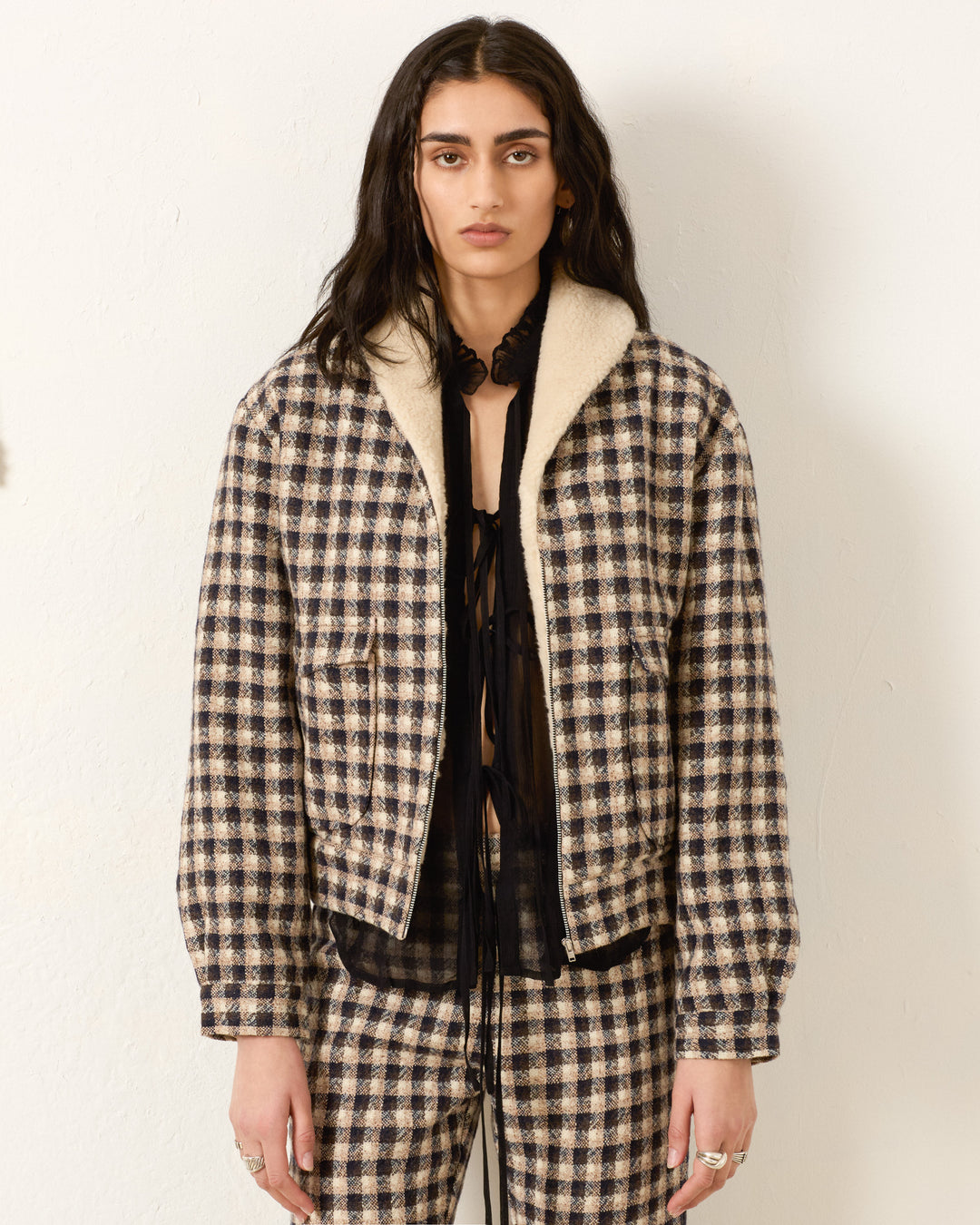 Wearing the Eli Trail Dust Bomber Jacket and matching plaid pants, the person stands against a plain off-white wall, looking directly at the camera.