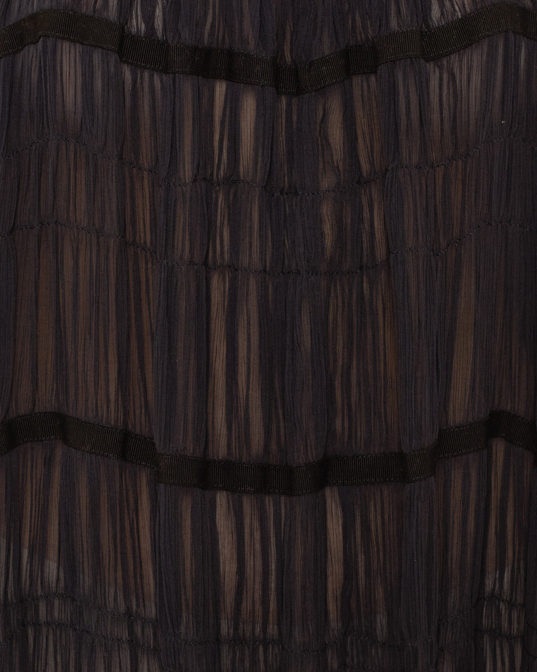Close-up of sheer black pleated fabric with horizontal bands creating ruched tiers, highlighting the elegant detail of the Emrys Shadow Chiffon Dress.
