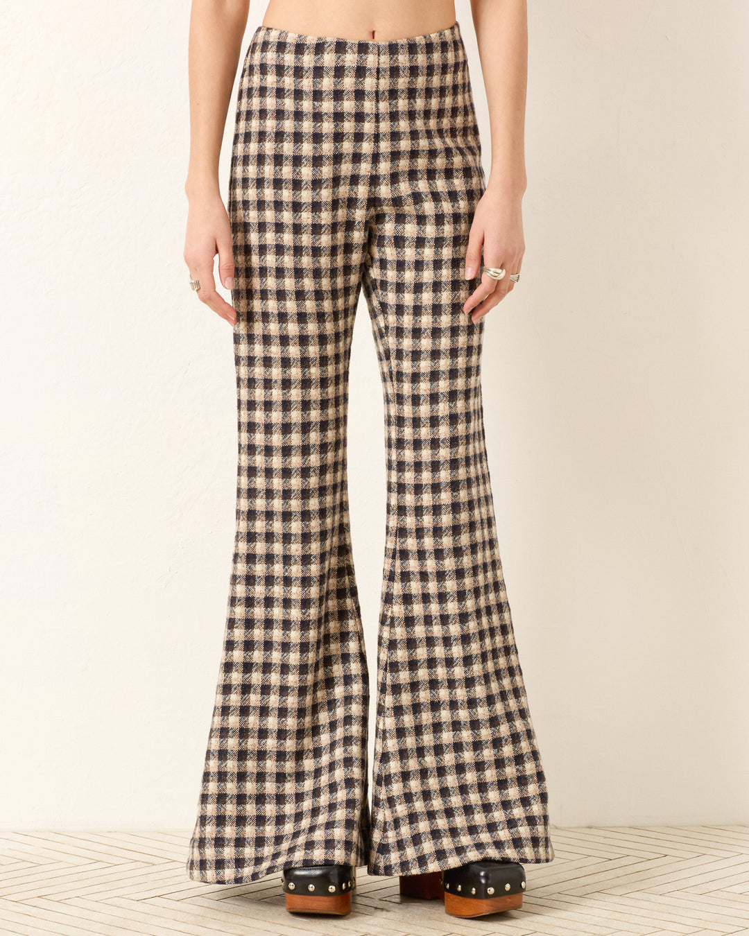 Person wearing the Farah Trail Dust Pant—plaid high-waisted bell-bottoms in Italian virgin wool with a beige and black check pattern—paired with black platform clogs.