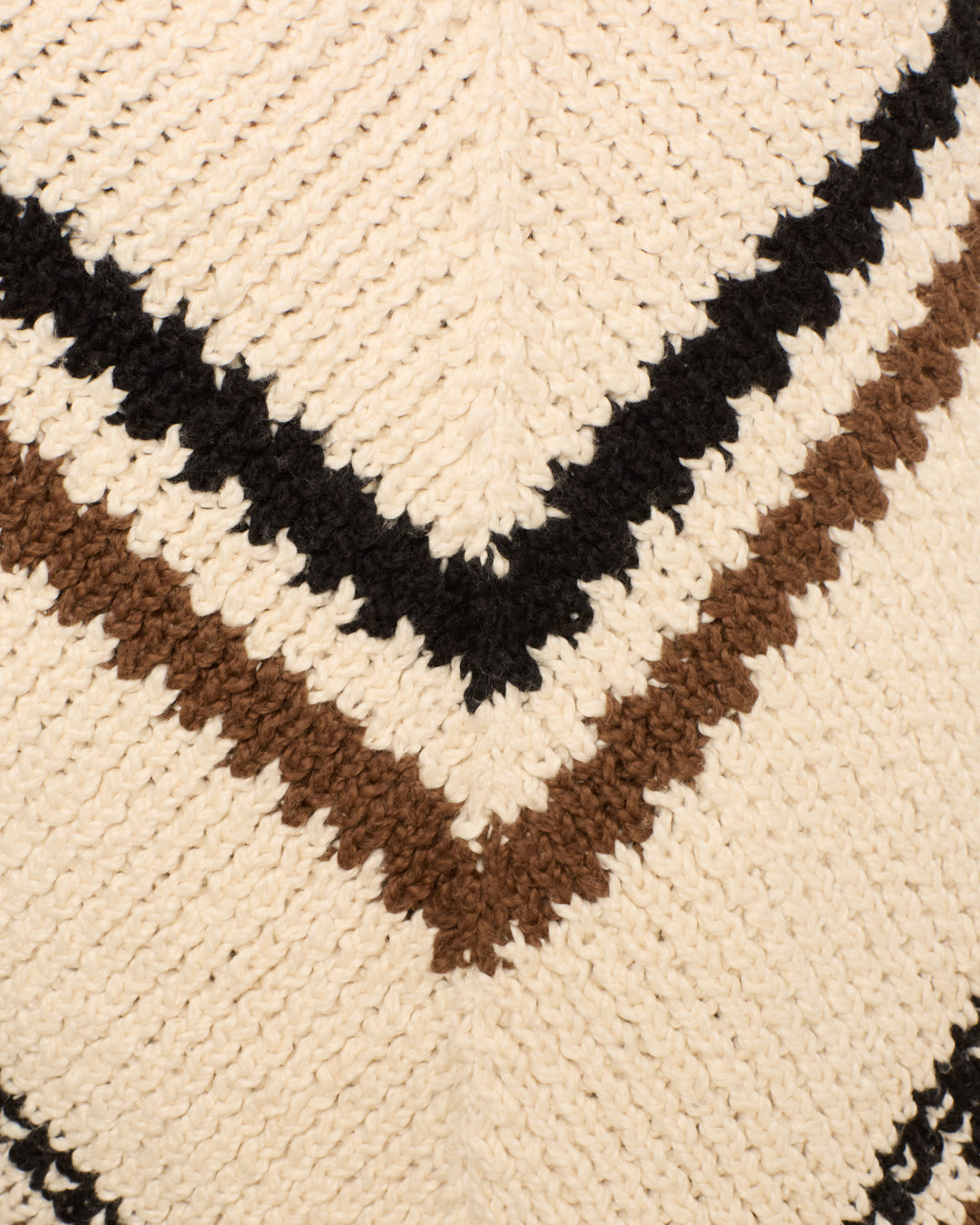 Close-up of the Faune Rawhide Knit Poncho, showcasing cream, brown, and black zigzag stripes in a chevron pattern.