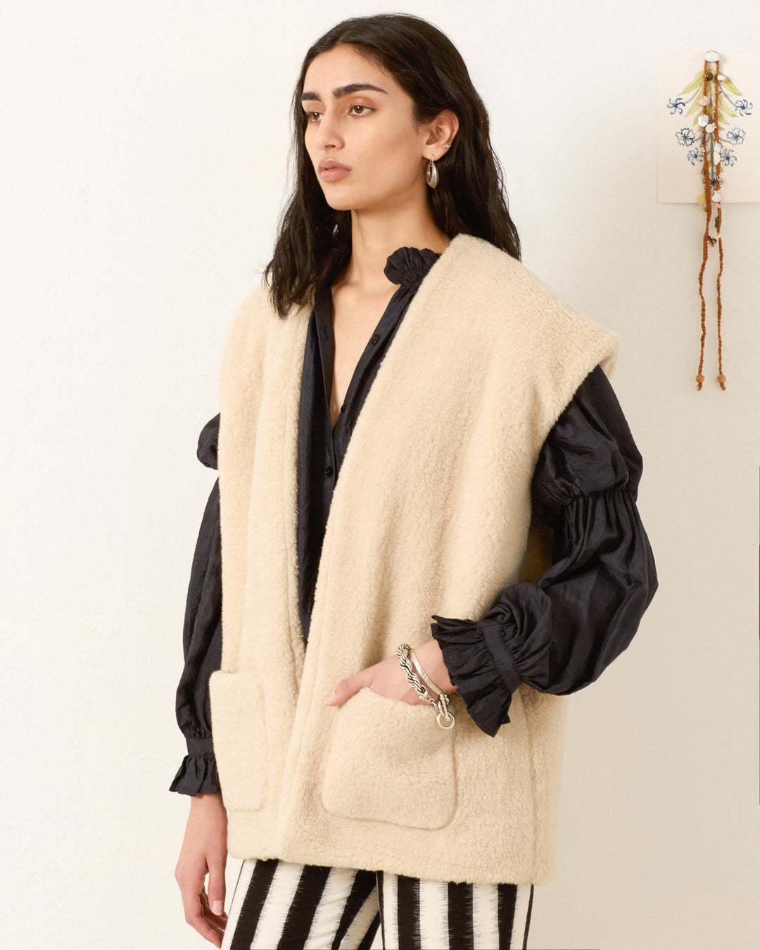 A person wears the cream Harrow Cactus Spur Vest over a black puff-sleeve blouse and black-and-white striped pants, standing against a neutral wall.