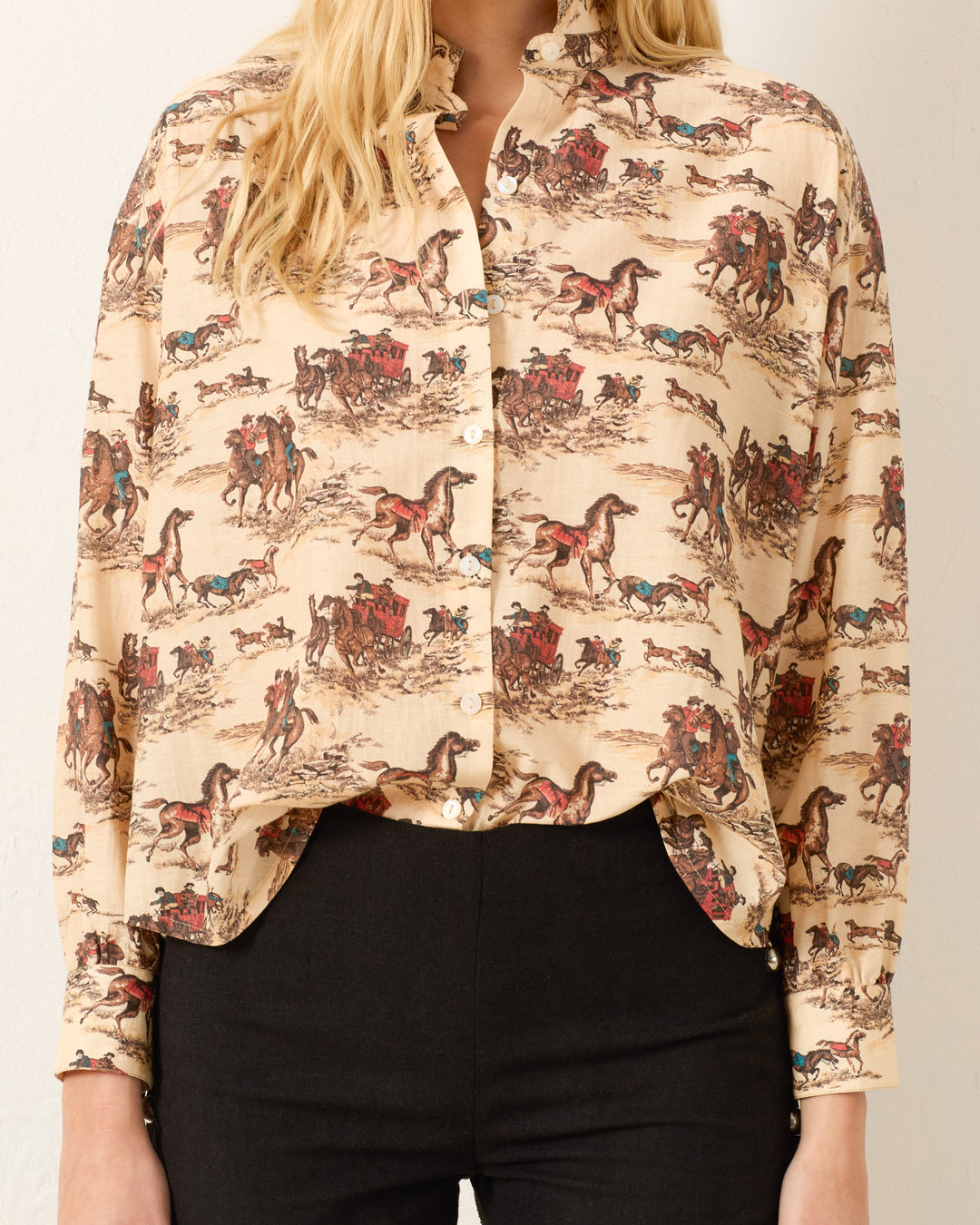 A person wearing the Kiki Canyon Cowboy Shirt in beige with a multicolored horse and western scene print, paired with black pants.