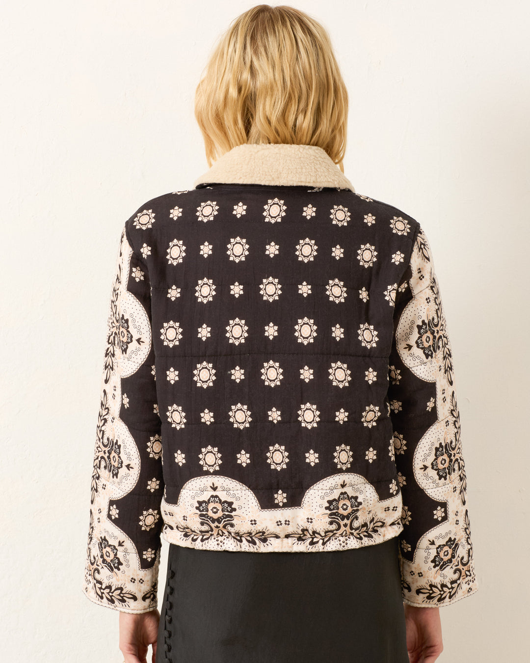 A person with blonde hair faces away, wearing the Lex Bronco Bandana Jacket featuring black and beige bandana prints with floral and geometric designs.