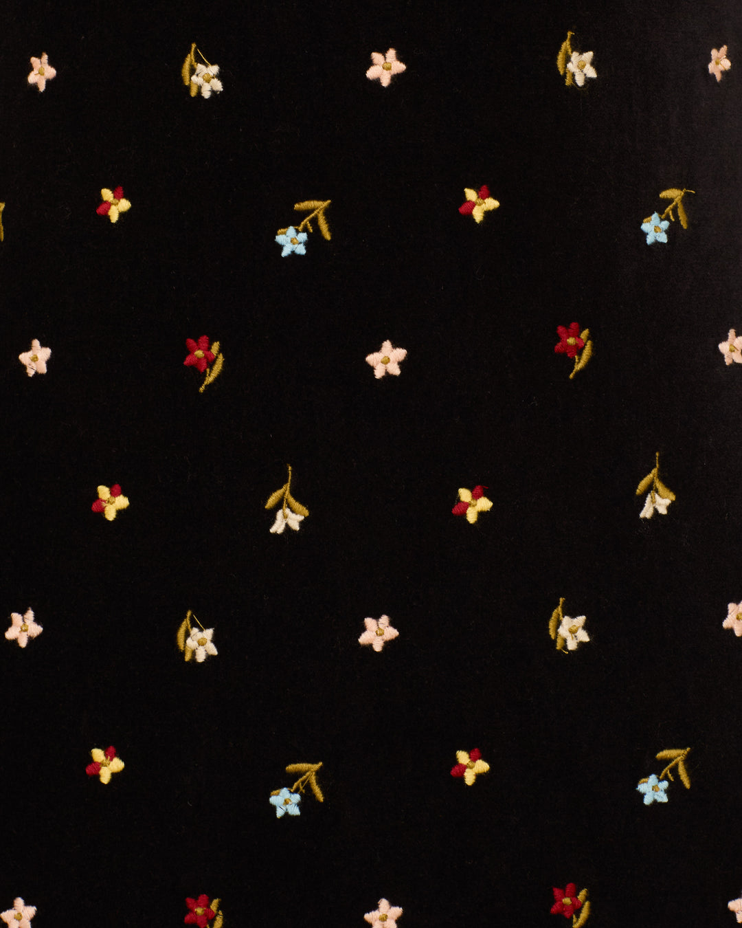 The Romy Onyx Bouquet Dress is a black cotton-velvet mini dress adorned with small embroidered red, yellow, blue, and white flowers throughout and finished with long flared sleeves.
