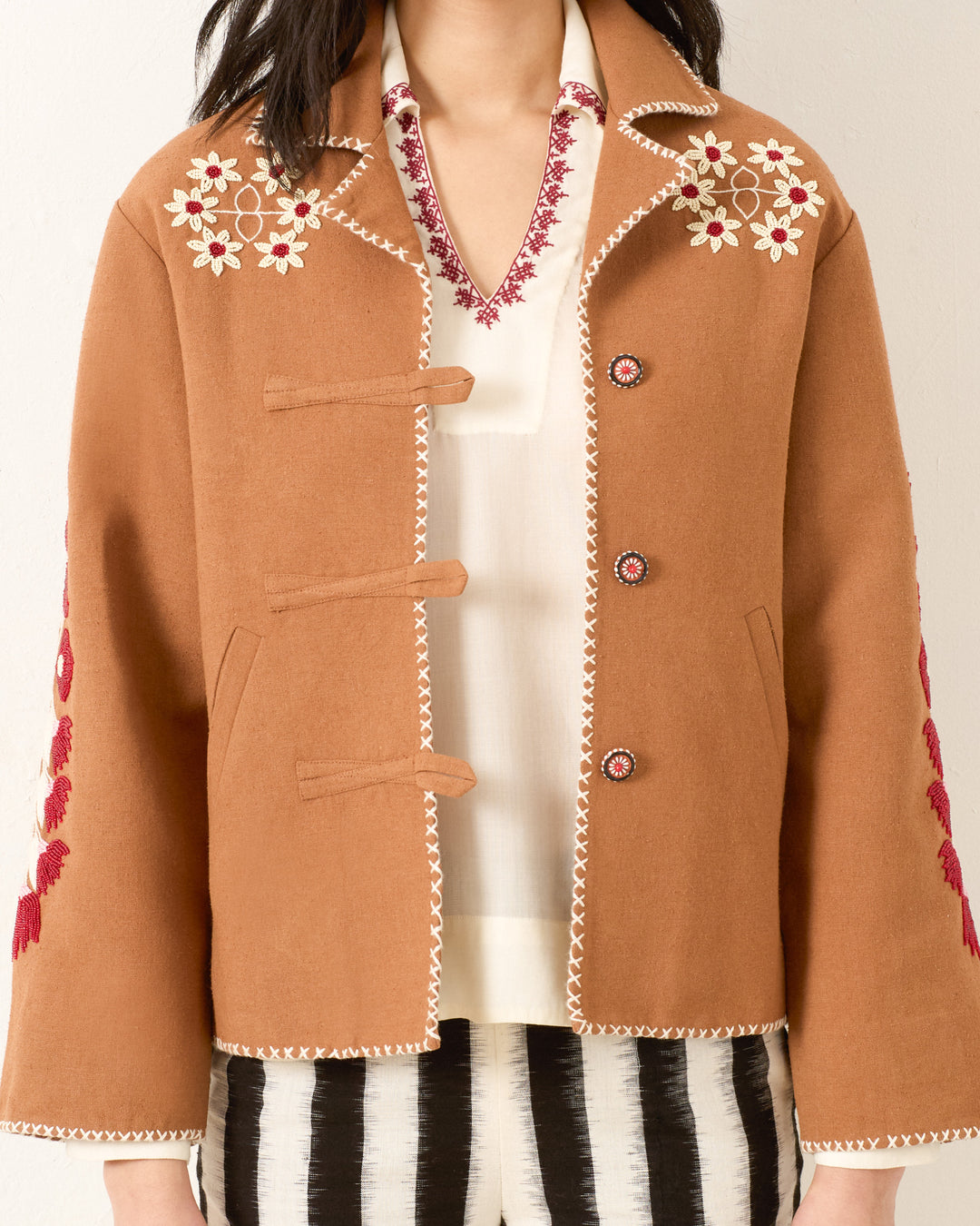 Wearing the Western Cactus Bloom Jacket, featuring floral embroidery on the shoulders and sleeves, over a white shirt with red embroidery and paired with black and white striped pants.