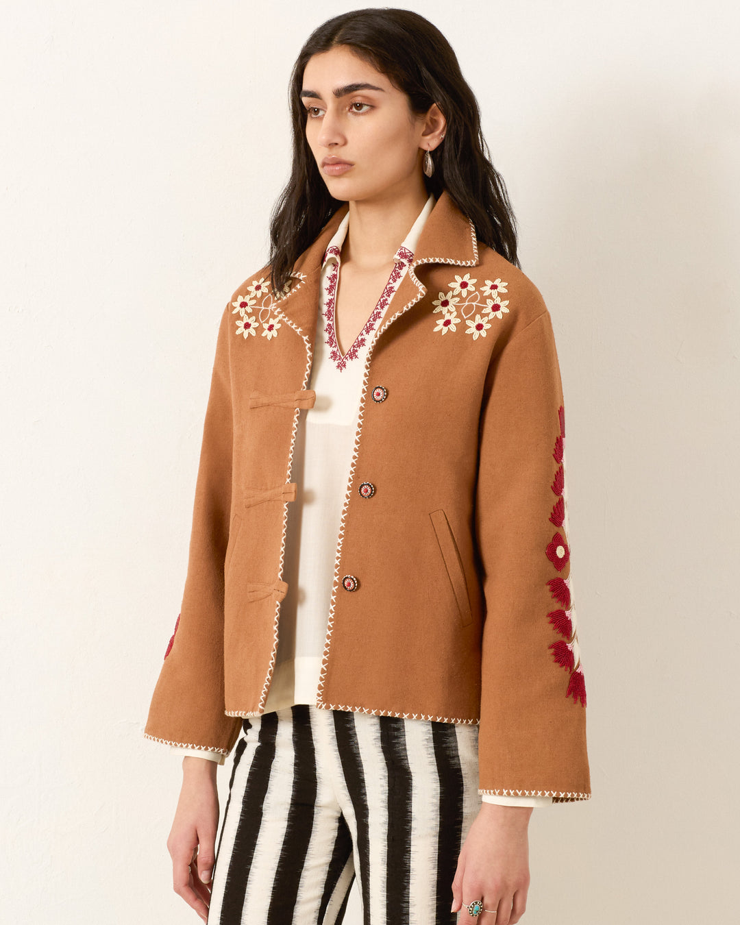 A woman wears the Western Cactus Bloom Jacket with white and red embroidery over a white top and black-and-white striped pants, standing against a plain background.