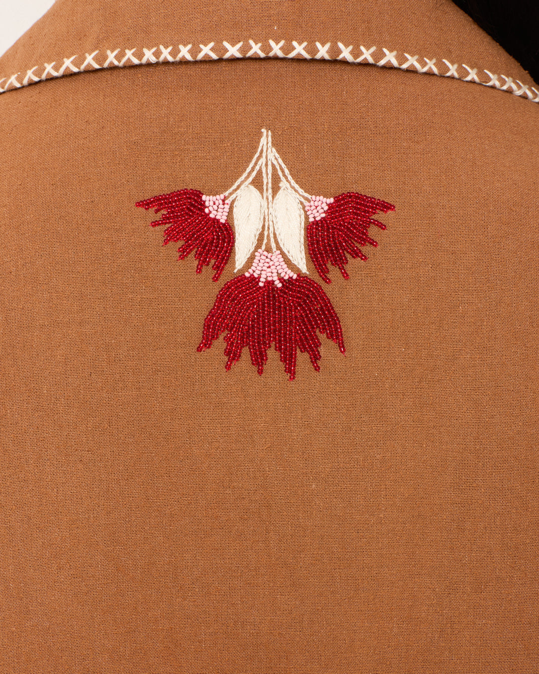 Close-up of the Western Cactus Bloom Jacket in brown, featuring a stitched white X on the collar and a red and white hand-beaded floral motif below it.