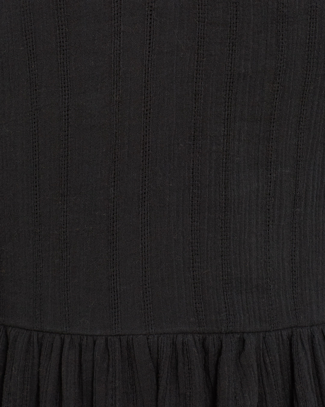 Close-up of black textured fabric with vertical ribbed lines and gathered detailing at the bottom, featured on the Winslow Shadow Lace Dress—a chic choice for holiday parties.
