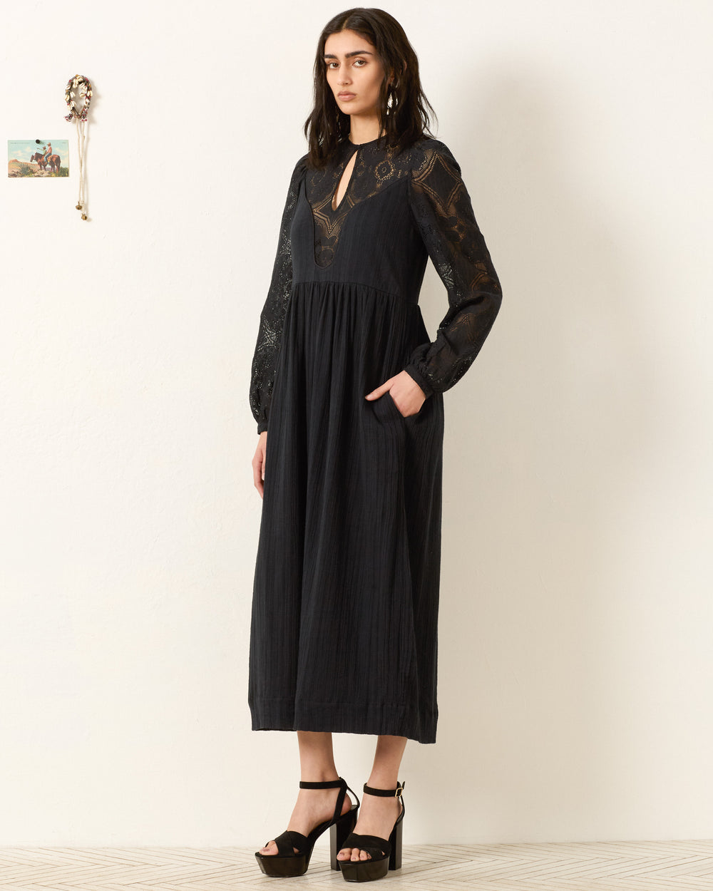 A woman in the Winifred Shadow Lace Dress, a black maxi featuring elegant floral lace, perfect for holiday parties.