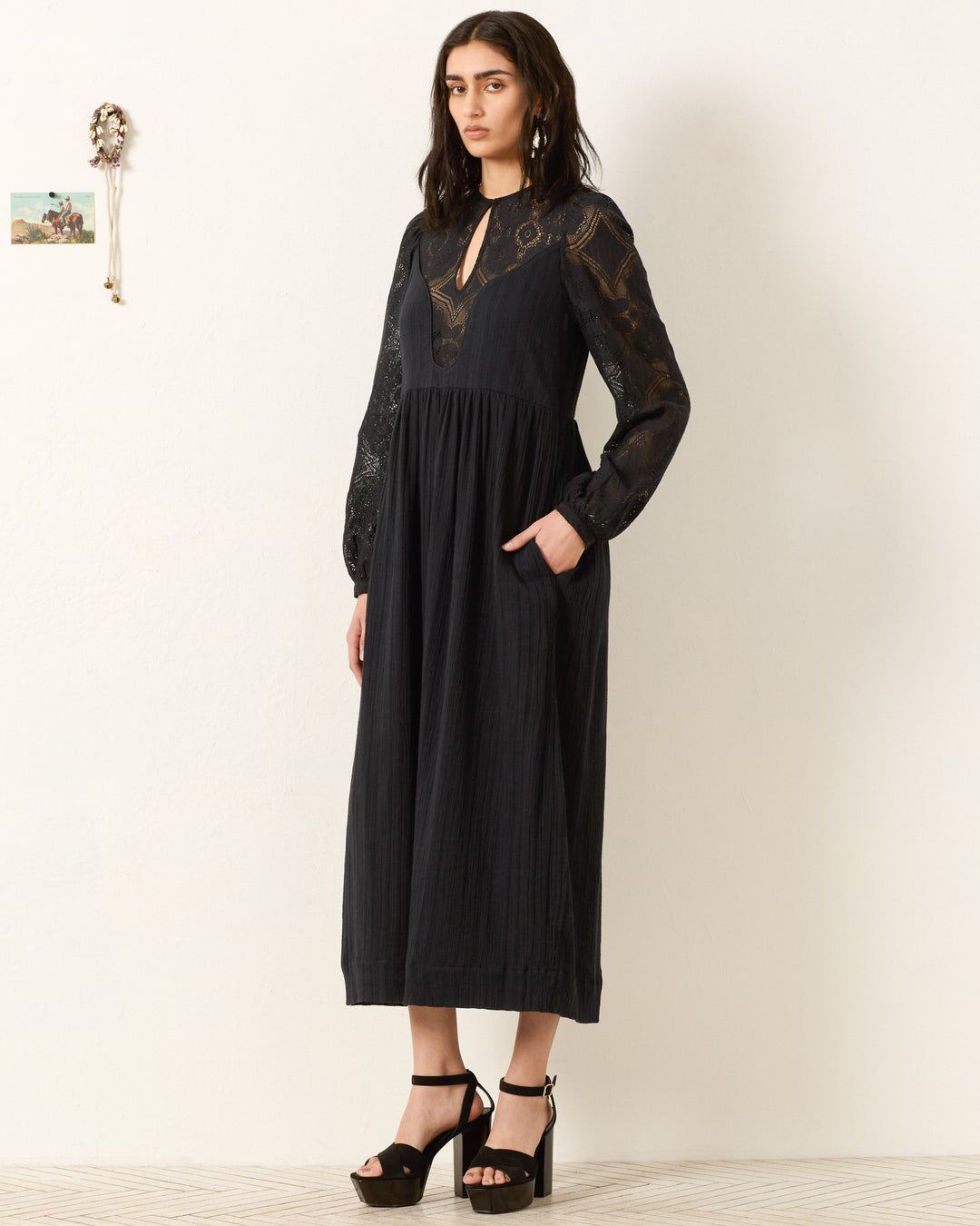 A woman in the Winifred Shadow Lace Dress, a black maxi featuring elegant floral lace, perfect for holiday parties.
