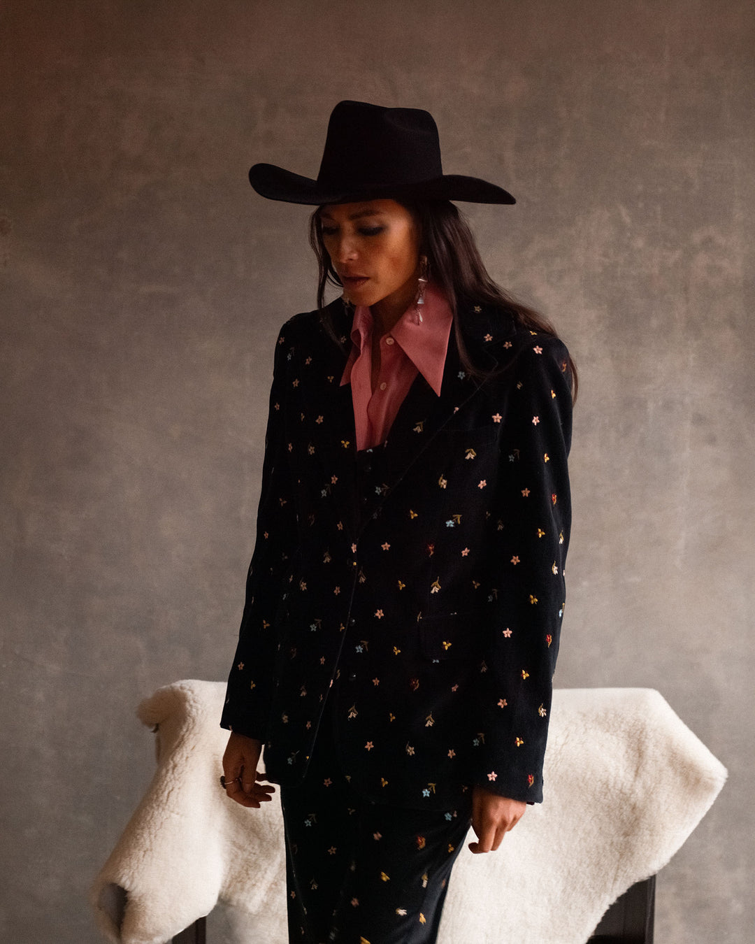 Wearing the Charlie Onyx Bouquet Pant, a woman in a cowboy hat showcases bold floral embroidery and adds Western flair to her look.
