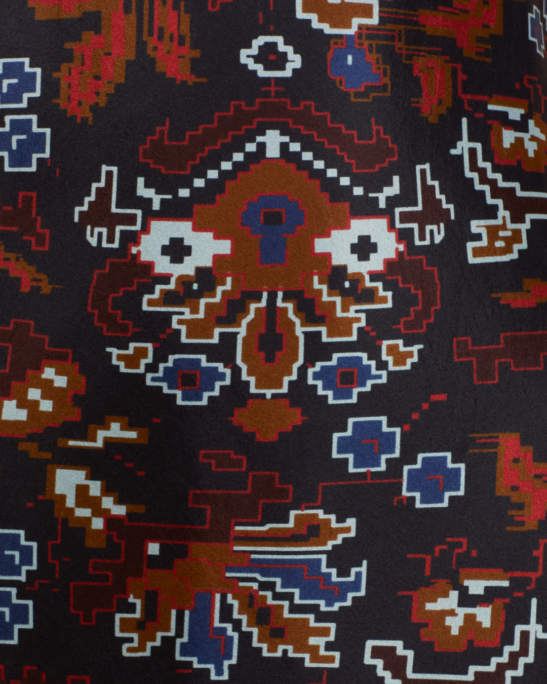 Close-up of the Adele Indigo Kilim Silk Dress fabric, showcasing a geometric, pixel-art-inspired pattern in red, brown, blue, white, and black colors with kilim-inspired motifs.