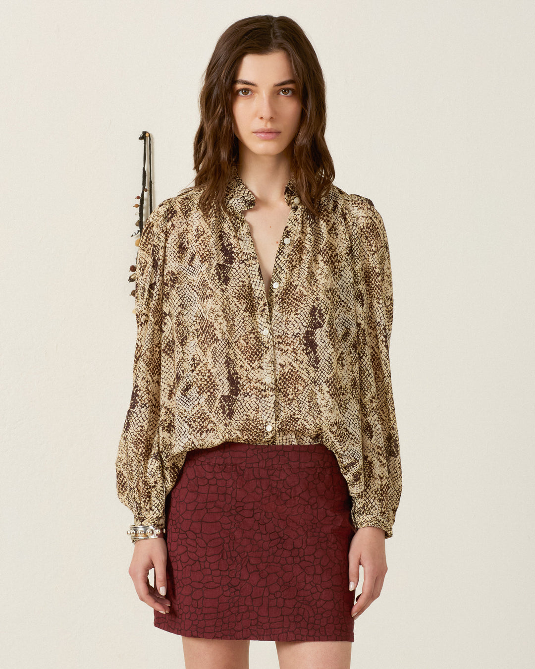 A woman stands against a plain background, wearing the Annabel Lemon Snakeskin Shirt with a ruffled collar and puff shoulders, paired with a maroon textured skirt. She looks directly at the camera with a neutral expression.
