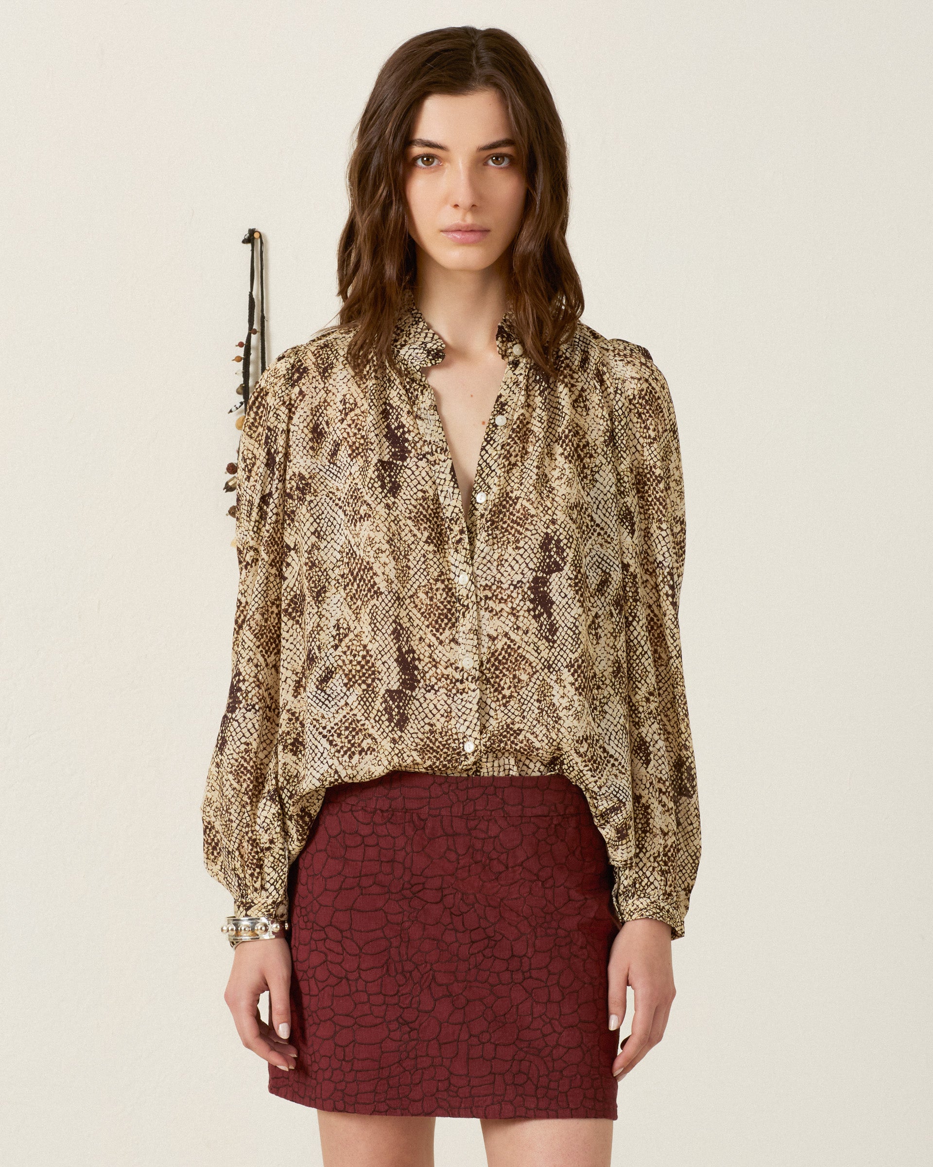 A woman stands against a plain background, wearing the Annabel Lemon Snakeskin Shirt with a ruffled collar and puff shoulders, paired with a maroon textured skirt. She looks directly at the camera with a neutral expression.
