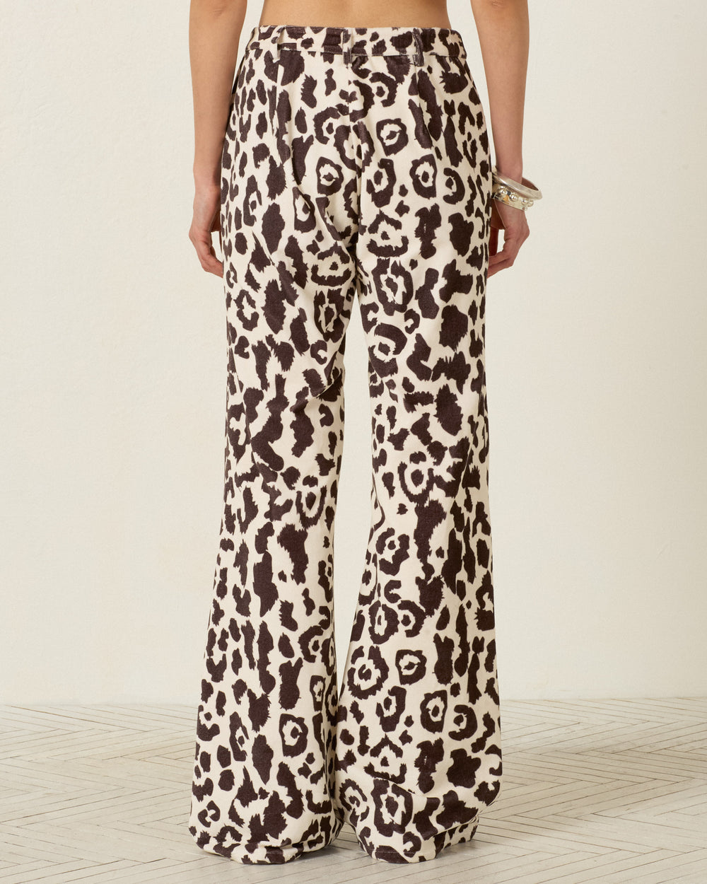 A person is shown from the back standing on a light-colored floor, wearing the Bunny Leopard Steppe Jean—high-waisted pants featuring a black and white leopard print and flared legs.