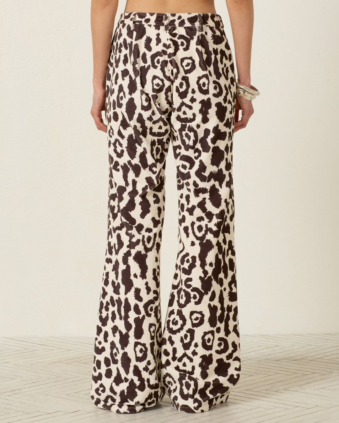 A person is shown from the back standing on a light-colored floor, wearing the Bunny Leopard Steppe Jean—high-waisted pants featuring a black and white leopard print and flared legs.
