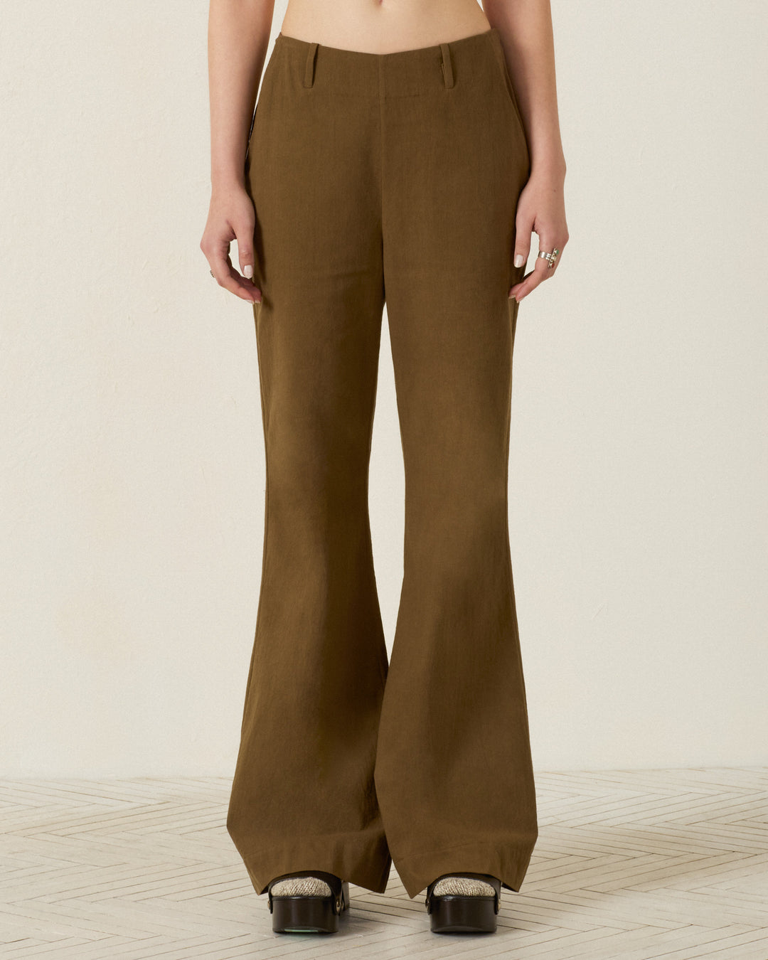 Person wearing the Charlie Olive Branch Pant—high-waisted, wide-leg pants in brown Khadi cotton—paired with black platform shoes, standing against a light-colored background. Only the lower torso and legs are visible.