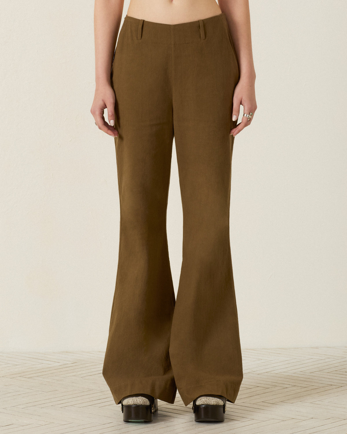 Person wearing the Charlie Olive Branch Pant—high-waisted, wide-leg pants in brown Khadi cotton—paired with black platform shoes, standing against a light-colored background. Only the lower torso and legs are visible.