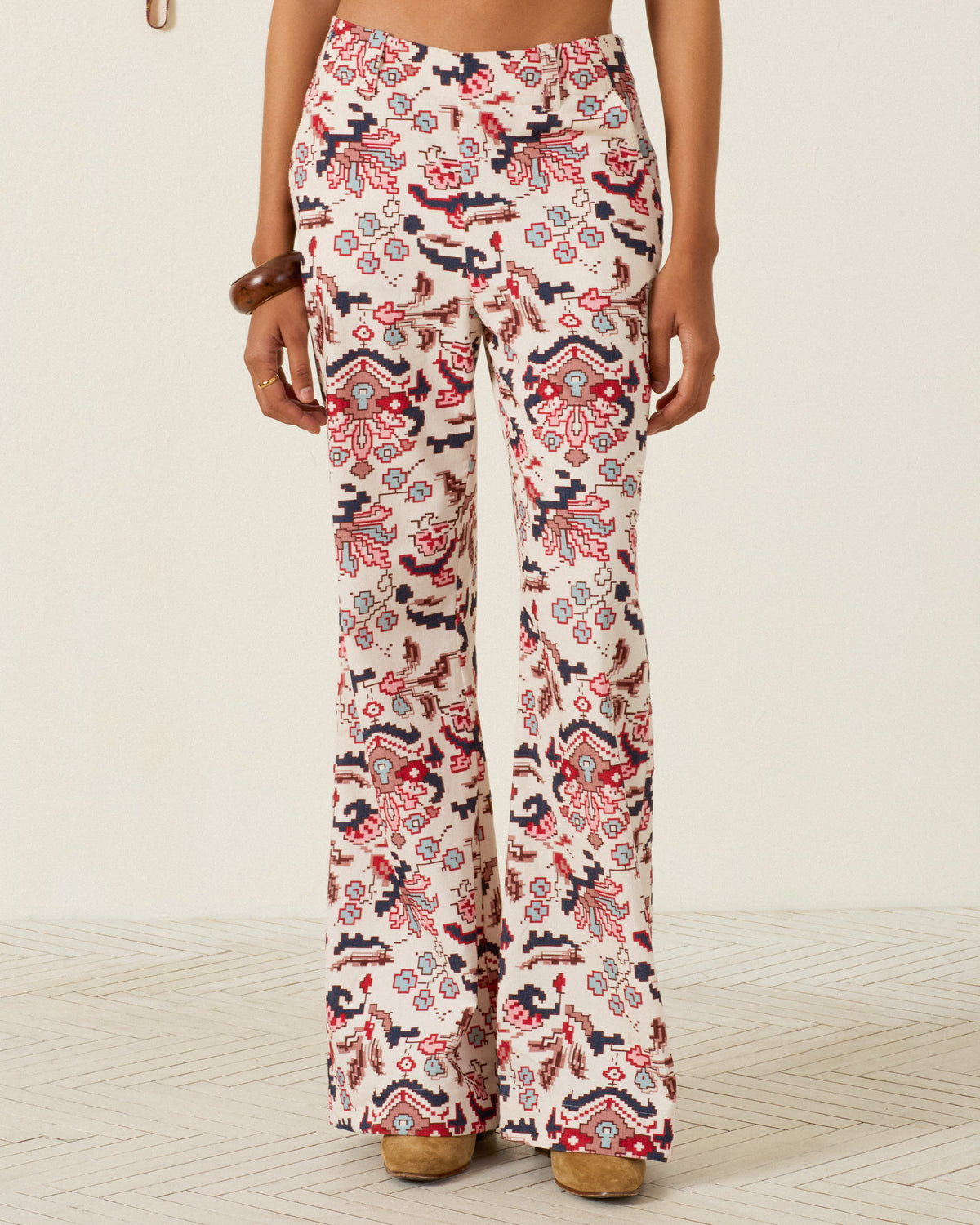 A person wearing the Charlie Horizon Kilim Pant, featuring a high-waisted, wide-leg silhouette with an intricate red and black kilim-inspired pattern, stands indoors on a light-colored floor.
