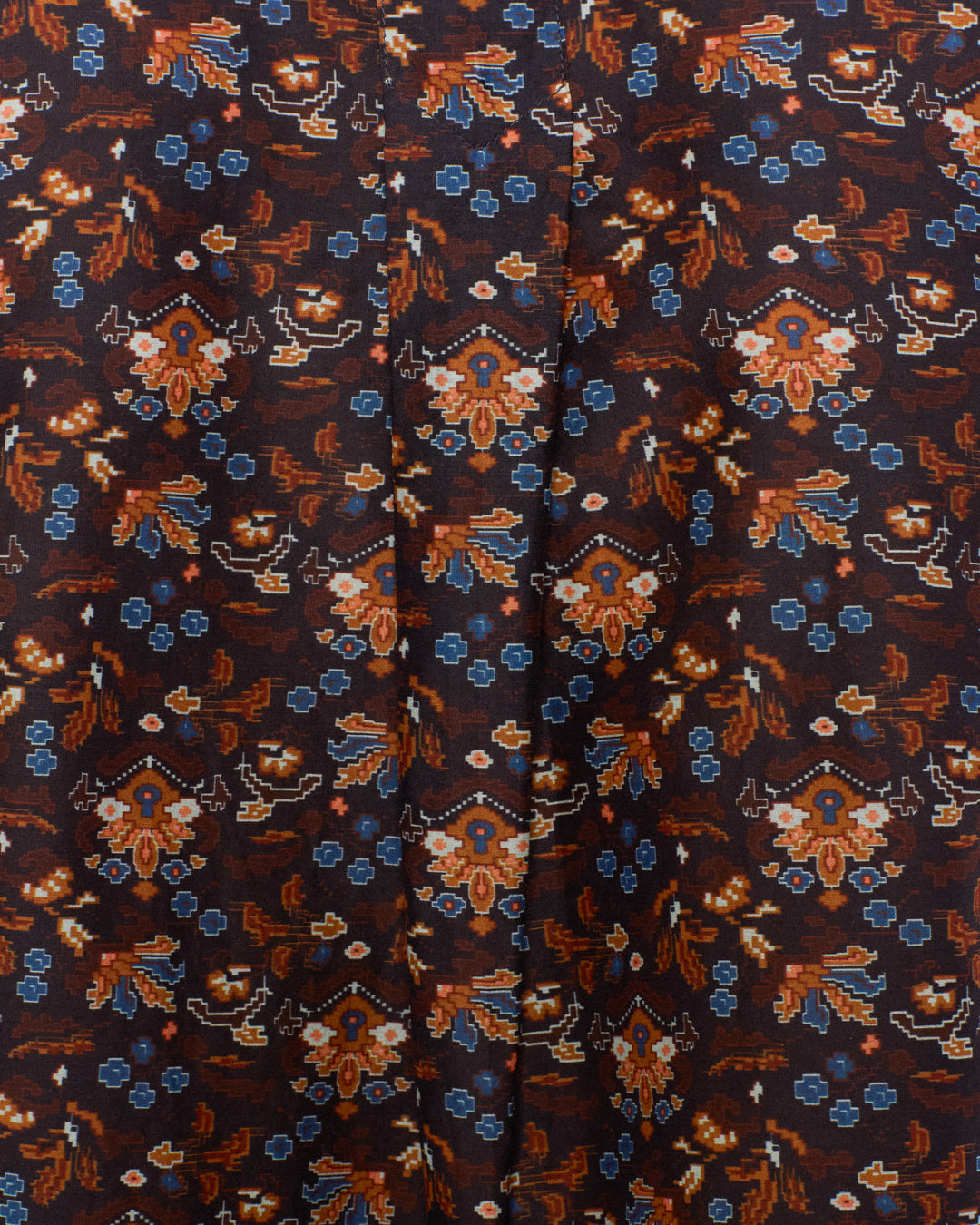 Close-up of the Molly Indigo Kilim Shirt, a cotton-silk blouse featuring intricate geometric and floral patterns in shades of brown, orange, and blue, with kilim-inspired motifs and a vertical central seam.