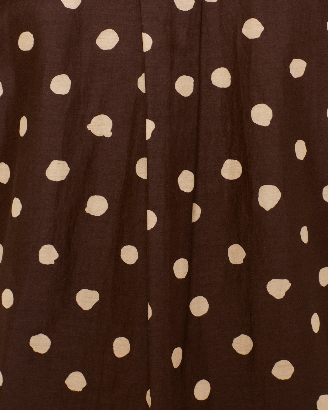 Close-up of the Molly Mahogany Dot Shirt, featuring a brown cotton-silk blend fabric with an irregular white polka dot pattern and vertical creases running down the surface, reminiscent of a chic polka-dot blouse.